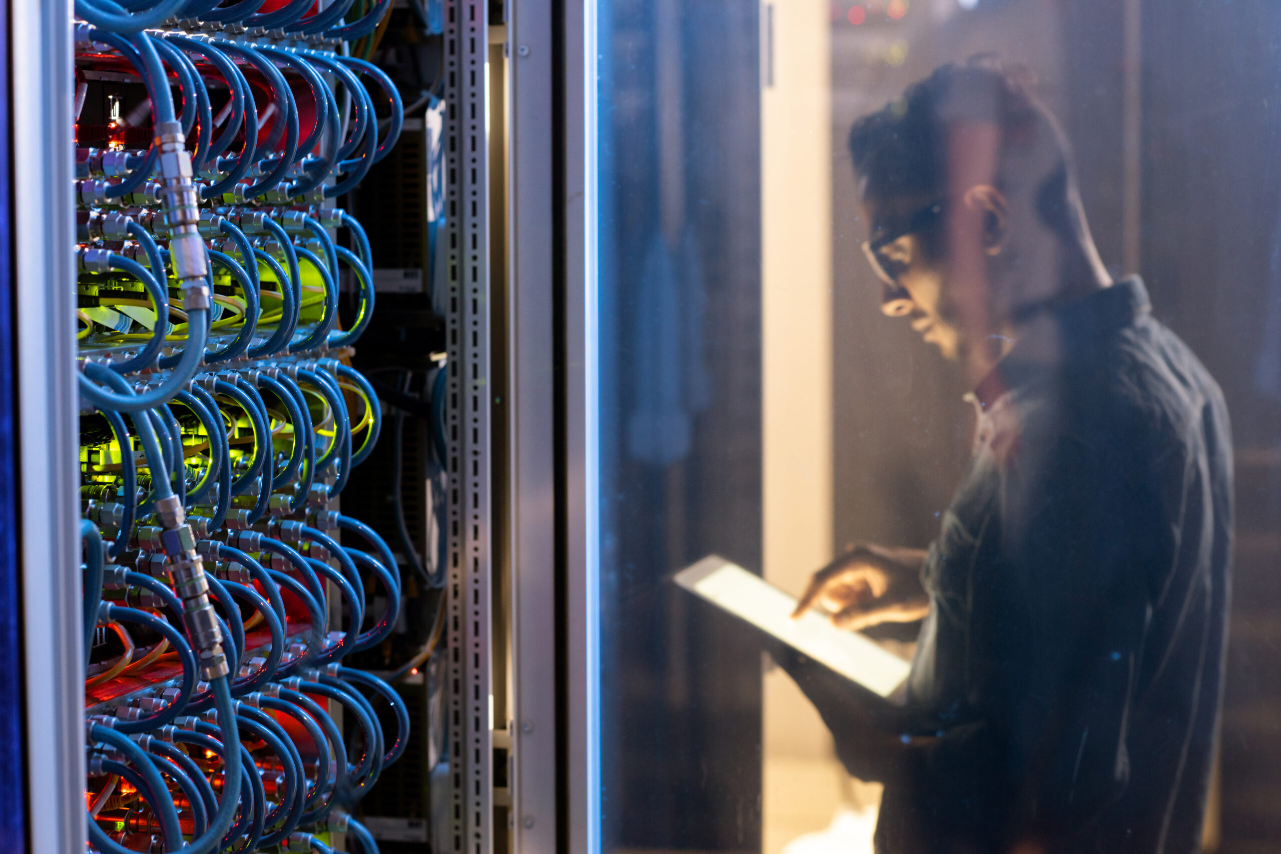 IT engineer testing new supercomputer while using digital tablet app, focus on open supercomputer cabinet with wires and cables